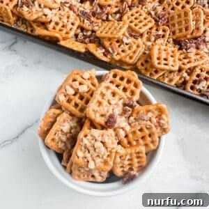 A close-up shot of a bowl filled with golden butter toffee pretzels, generously covered with scattered toffee bits and chopped pecans, highlighting the texture and glistening glaze.