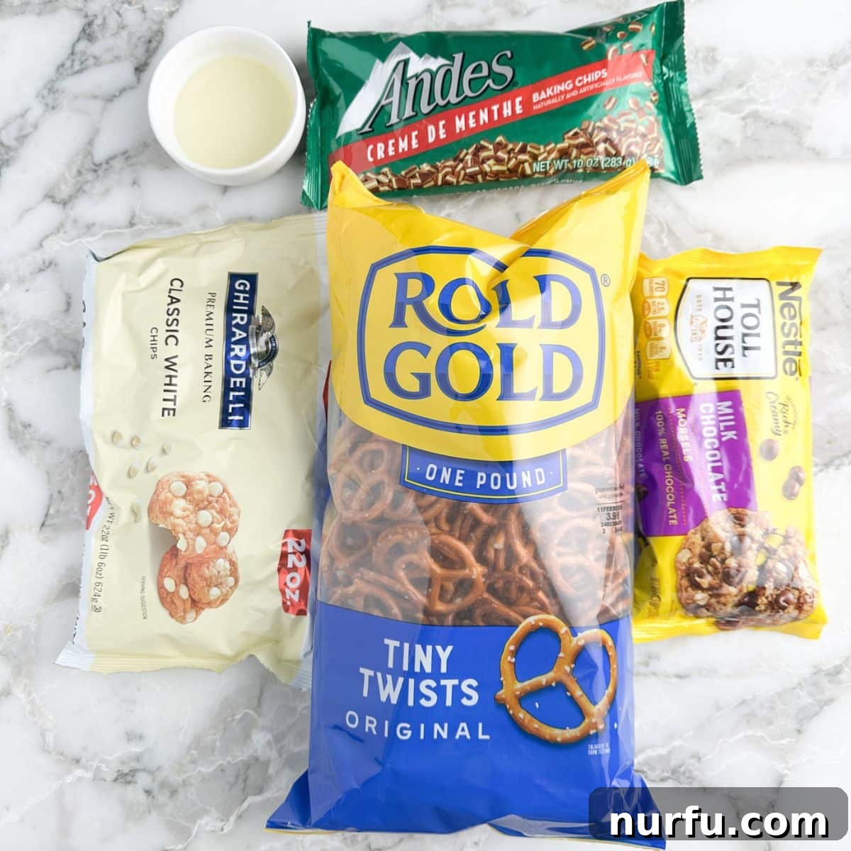 Andes Mint Chocolate Pretzel Crunch 3 A vibrant flat lay of key ingredients for Andes Mint Pretzel Bark, featuring a bag of mini pretzels, separate bowls of milk chocolate chips, white chocolate chips, and a mound of freshly chopped Andes Mints, all ready for assembly.