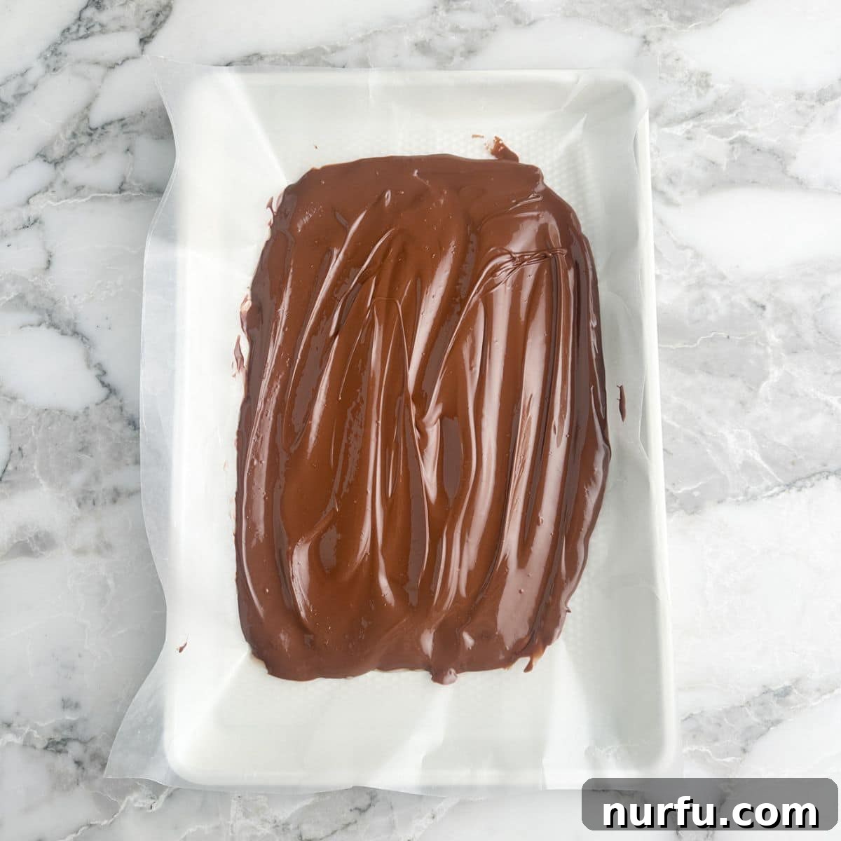 Andes Mint Chocolate Pretzel Crunch 5 A pristine layer of melted milk chocolate evenly spread on wax paper, creating the first smooth and inviting base layer for the upcoming pretzel bark, ready for toppings.