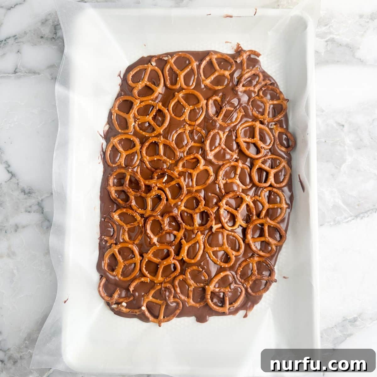 Andes Mint Chocolate Pretzel Crunch 6 Crisp mini pretzels neatly arranged and adhered on top of the set milk chocolate layer, forming the crunchy core of the Andes Mint Pretzel Bark, ready for the next indulgent step.