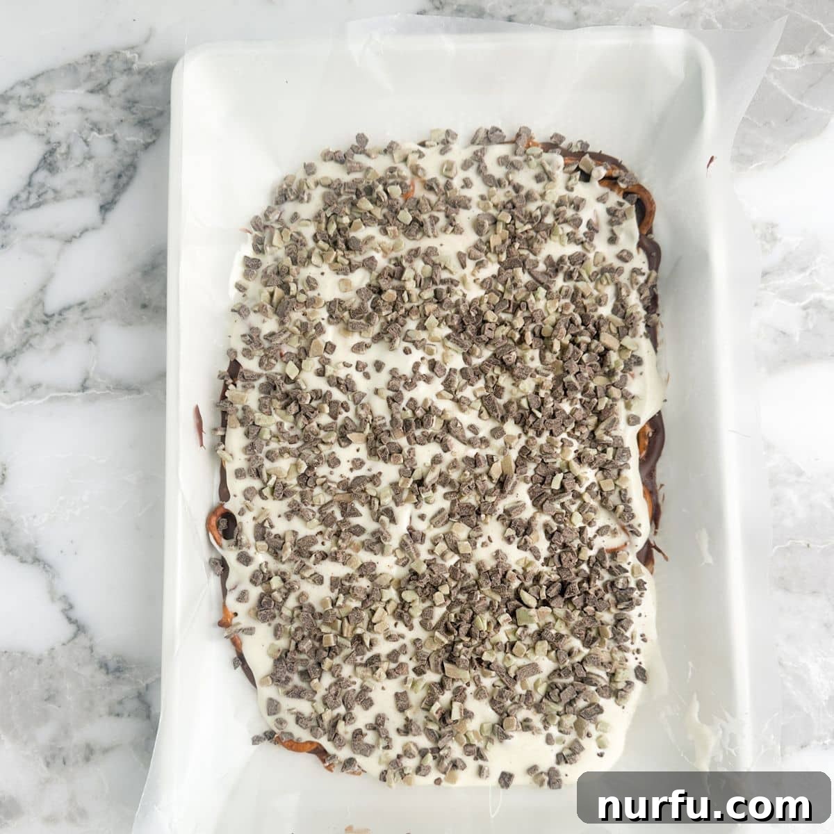 Andes Mint Chocolate Pretzel Crunch 8 A baking sheet showcasing the fully assembled Andes Mint Pretzel Bark, with vibrant layers of chocolate, pretzels, white chocolate, and a generous topping of Andes Mint pieces, hardening beautifully.