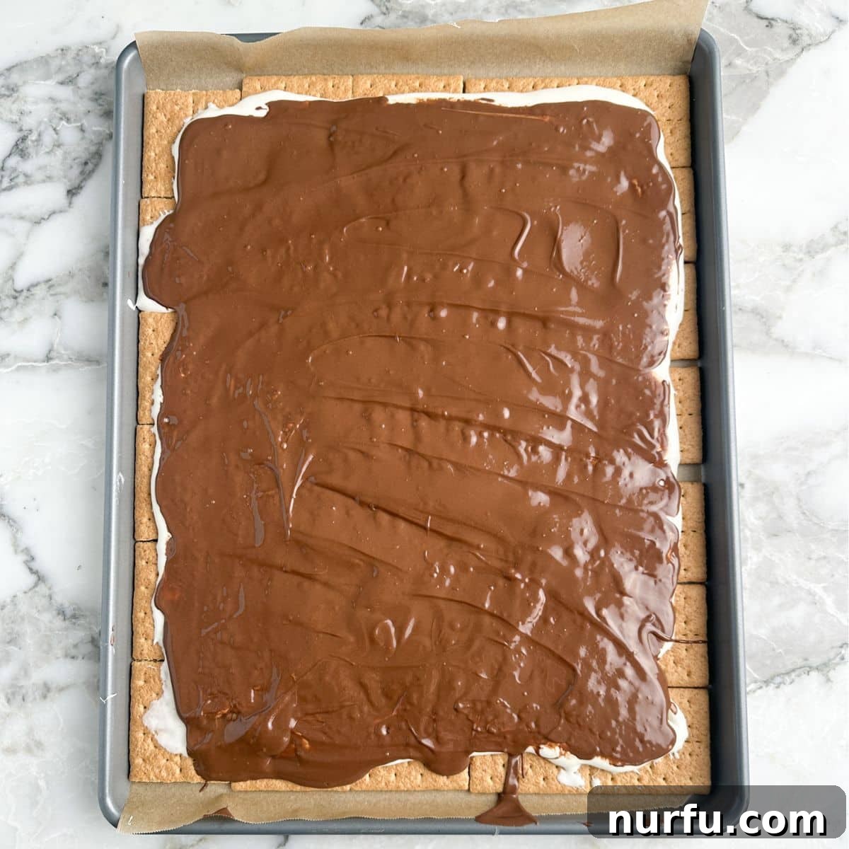Irresistible S'mores Bark 6 S'mores bark setting on a baking sheet, with visible layers of graham cracker, marshmallow, and chocolate.