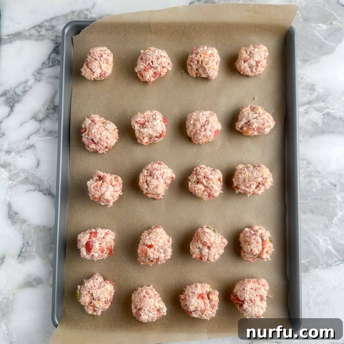 A baking sheet neatly lined with uncooked Rotel Cream Cheese Sausage Balls, perfectly portioned and ready for the oven.