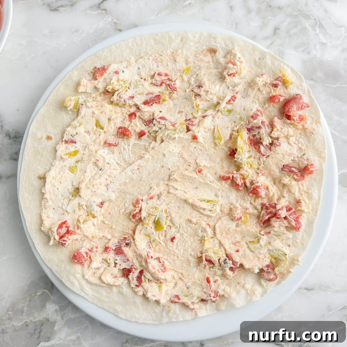 Italian Spiral Bites 5 A large tortilla with a generous layer of the seasoned cream cheese mixture spread across its surface.