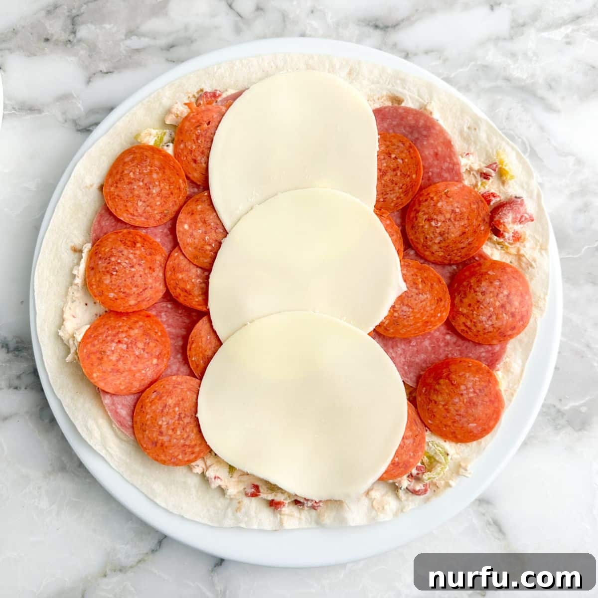 Italian Spiral Bites 7 A tortilla with layers of pepperoni, salami, and provolone cheese arranged neatly, ready for rolling.