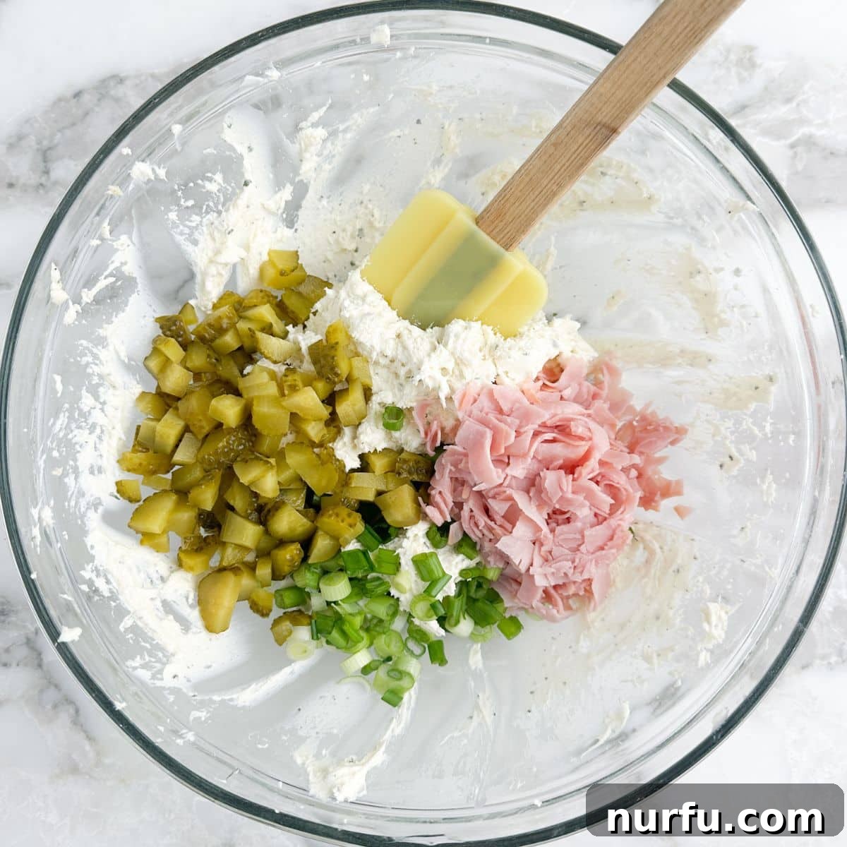 Creamy Dill Pickle Roll-Ups 5 A mixing bowl filled with the completed dill pickle pinwheel mixture: creamy cream cheese combined with chopped dill pickles, diced ham, and fresh green onions, all thoroughly mixed.