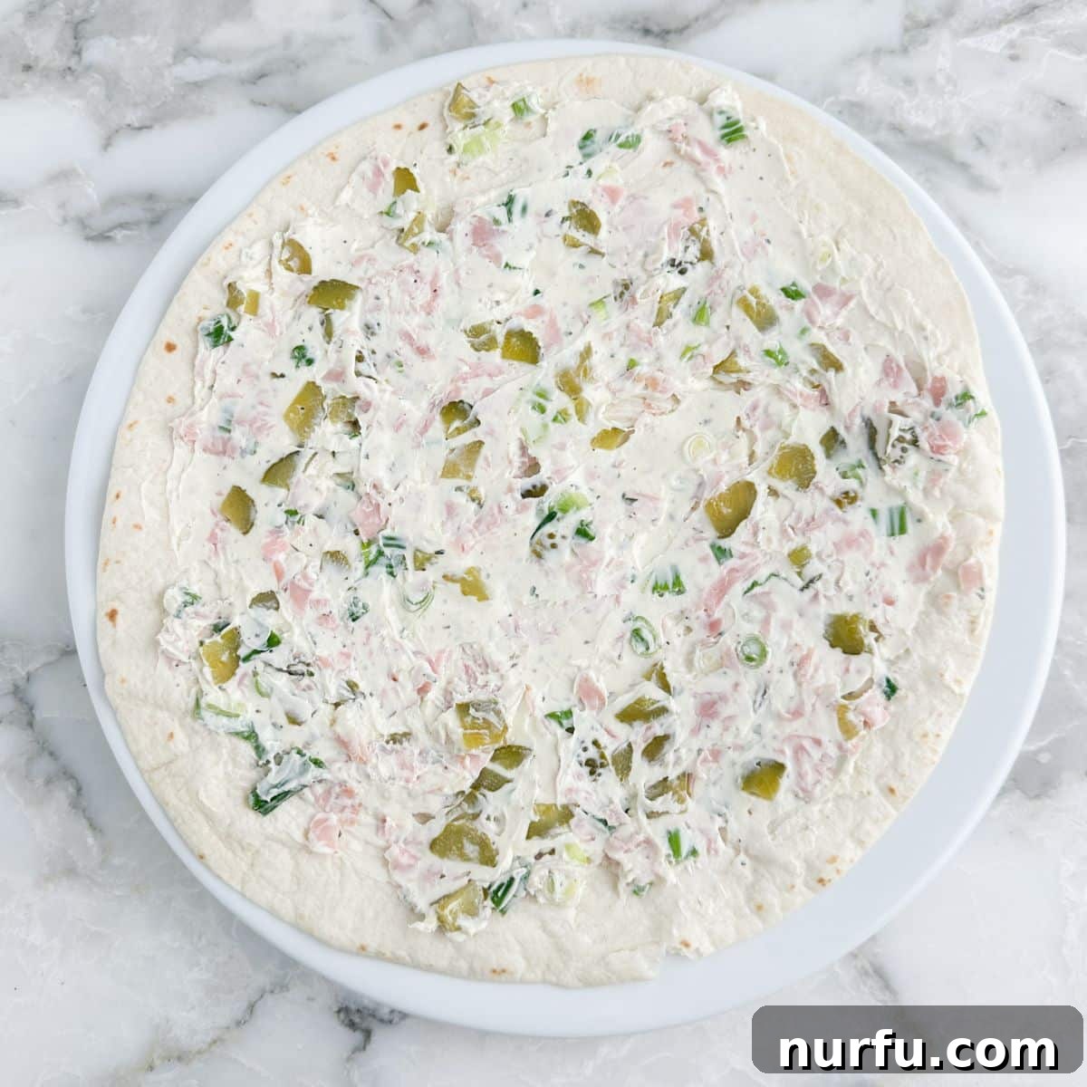 Creamy Dill Pickle Roll-Ups 6 A large flour tortilla meticulously covered with an even layer of the creamy dill pickle and ham mixture, ready for rolling.