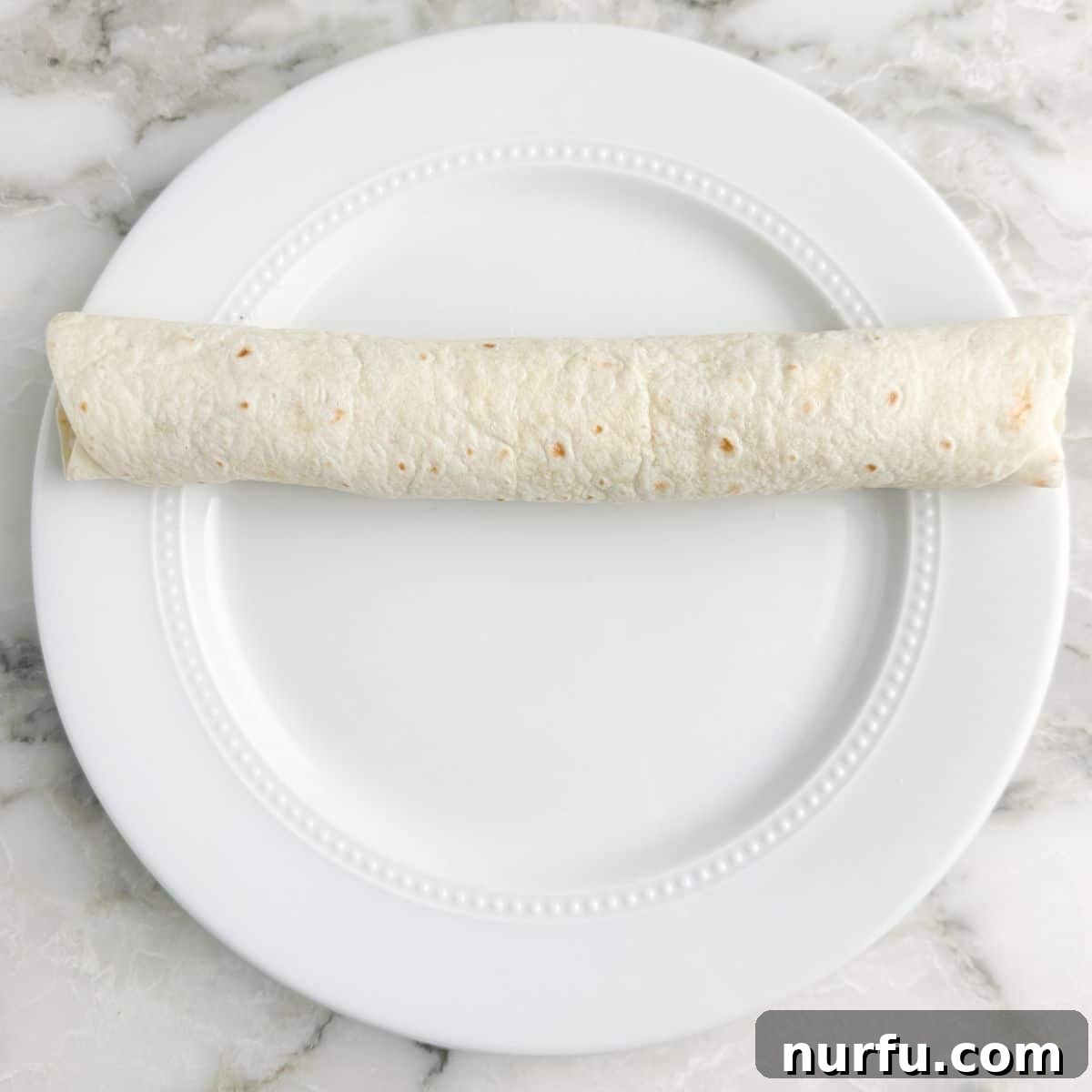 Creamy Dill Pickle Roll-Ups 7 A tightly rolled tortilla, filled with the creamy dill pickle mixture, resting on a plate and ready for chilling and slicing.