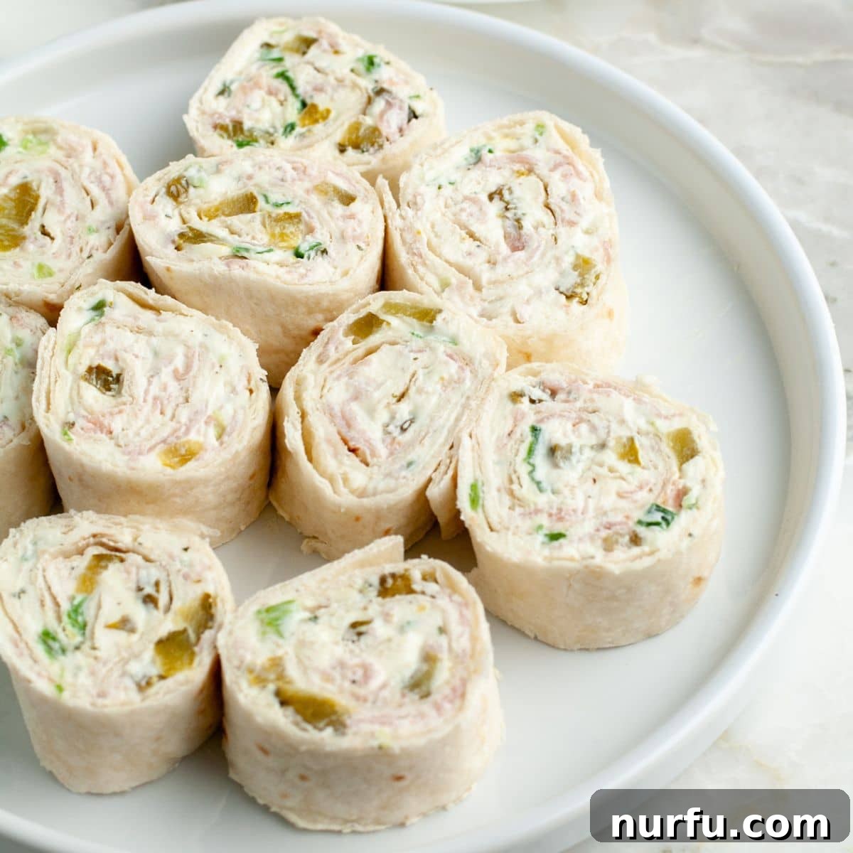 Creamy Dill Pickle Roll-Ups 8 A beautifully arranged platter of freshly sliced dill pickle pinwheels, showcasing their vibrant green and creamy white spirals, ready to be served.