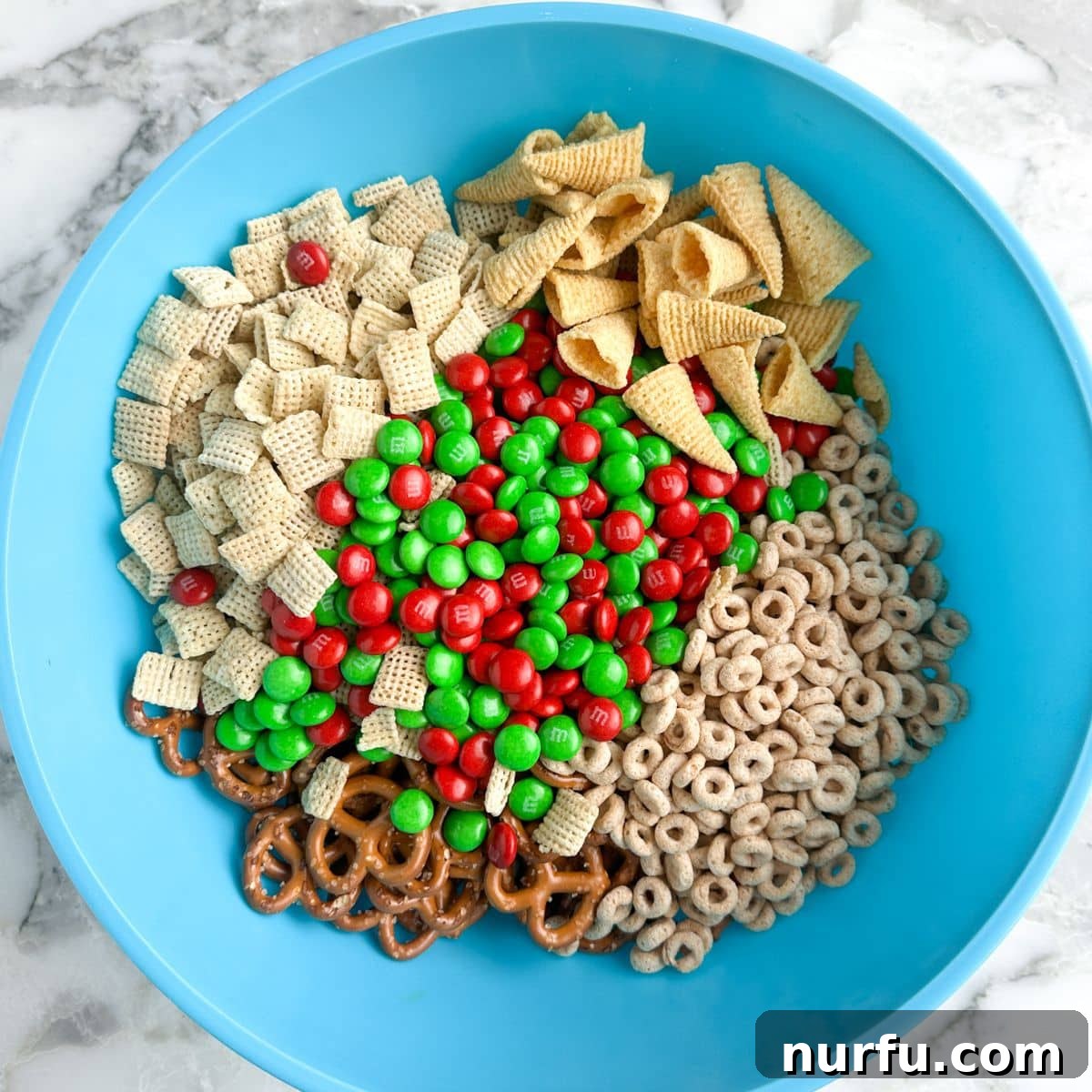 Festive Reindeer Treats 4 A large mixing bowl filled with a delightful medley of dry ingredients for Christmas reindeer crack, including colorful M&M's, various cereals, and crunchy pretzels and Bugles chips, all waiting to be coated in white chocolate.