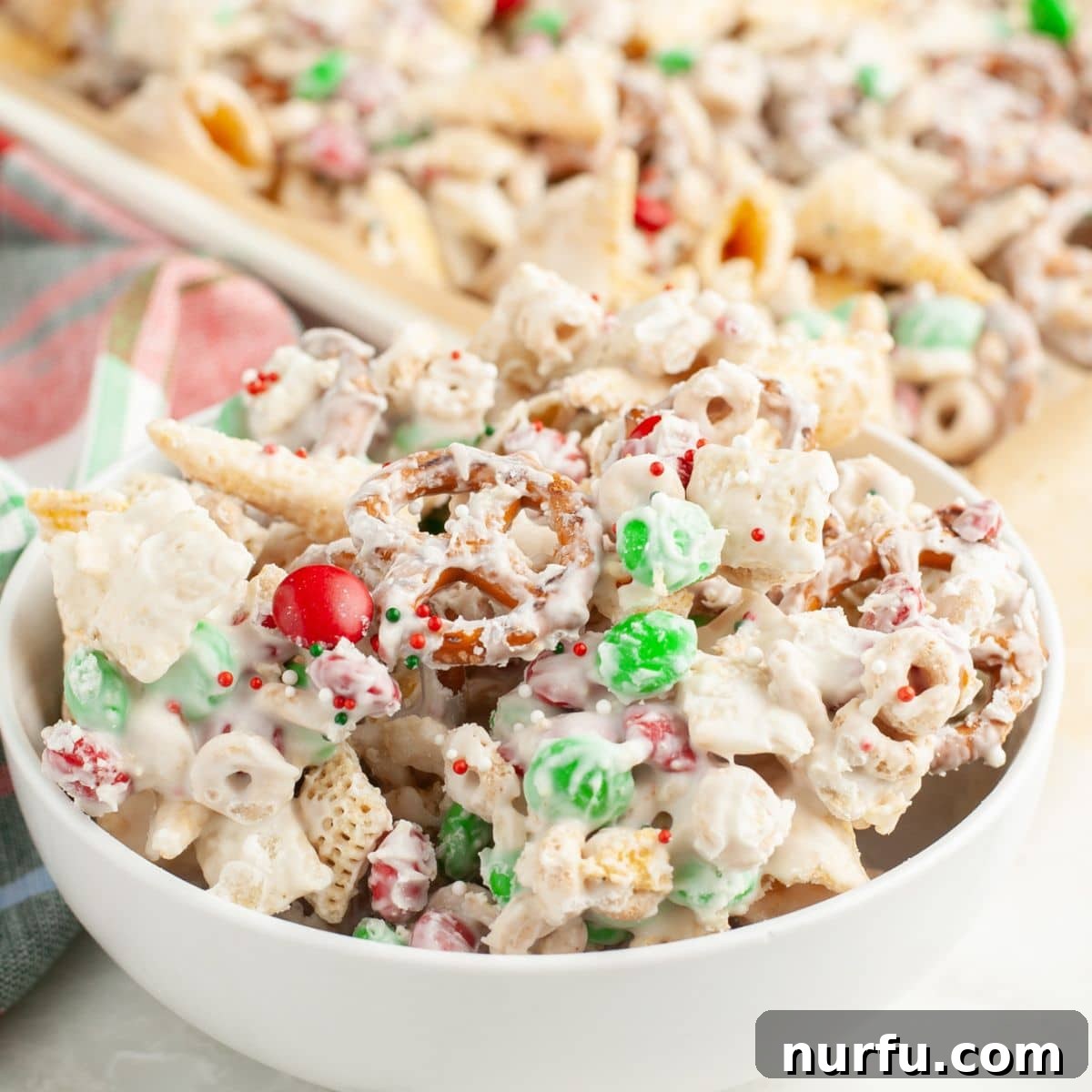 Festive Reindeer Treats 7 A festive bowl overflowing with delicious Christmas reindeer crack, showcasing the colorful M&M's, various cereals, pretzels, and Bugles chips, all coated in white chocolate and speckled with holiday sprinkles.