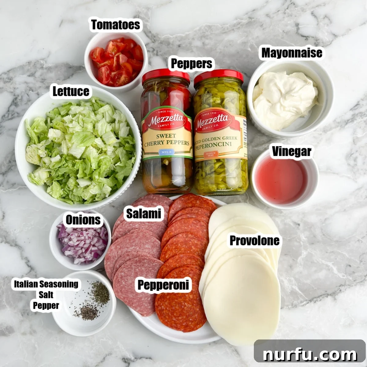 Stacked Hoagie Dip 3 All the fresh ingredients for hoagie dip laid out: chopped iceberg lettuce, sliced salami, pepperoni, provolone cheese, mayonnaise, red onion, and peperoncinis, ready to be combined.