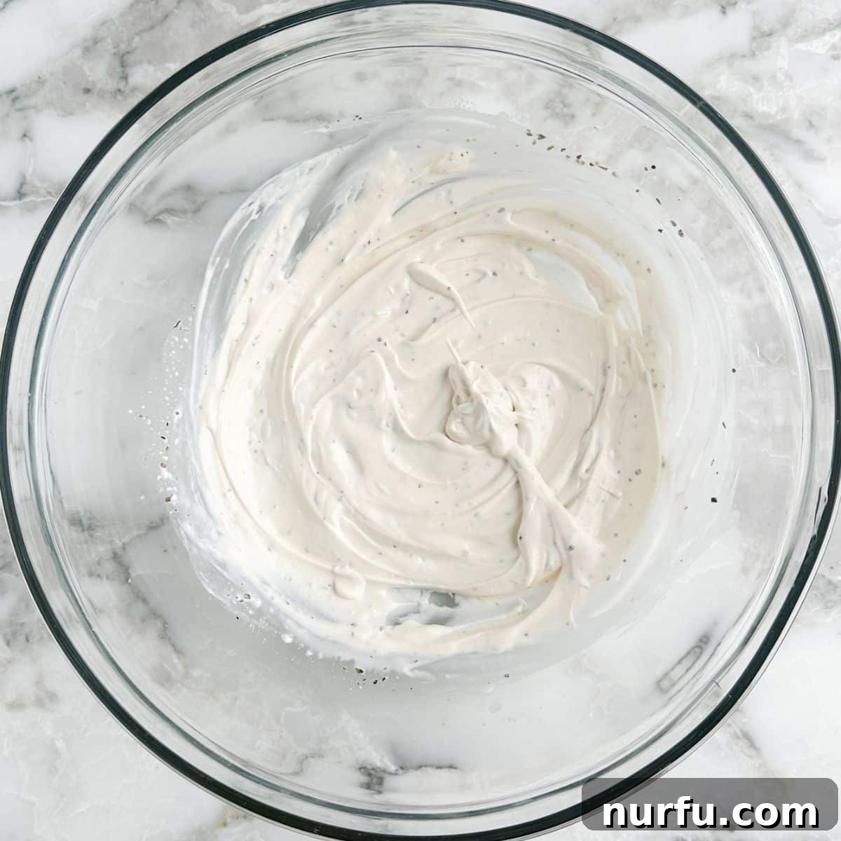 Stacked Hoagie Dip 4 A large glass bowl filled with a creamy, pale yellow Italian dressing, perfectly whisked and ready for the next steps in making the hoagie dip.