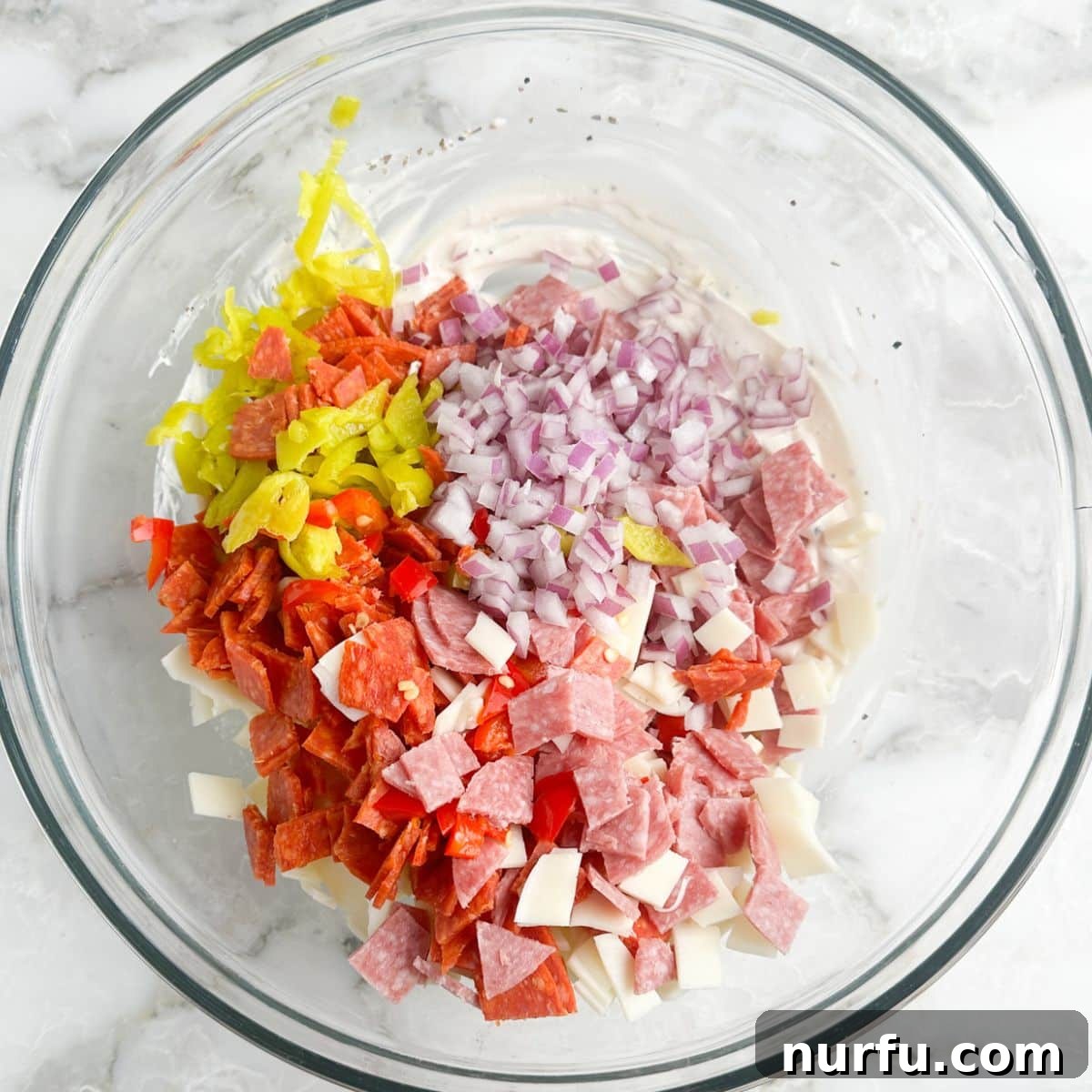 Stacked Hoagie Dip 5 A close-up shot of a bowl where diced salami, pepperoni, and red onion are being tossed with the creamy Italian dressing, starting to form the base of the hoagie dip.