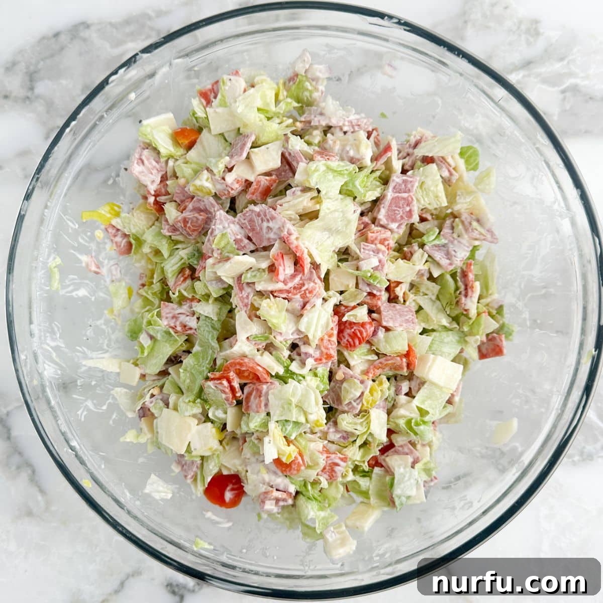 Stacked Hoagie Dip 6 A vibrant bowl of fully assembled hoagie dip, showcasing chopped lettuce, tomatoes, deli meats, and cheese, all coated in the creamy dressing and ready to be served.
