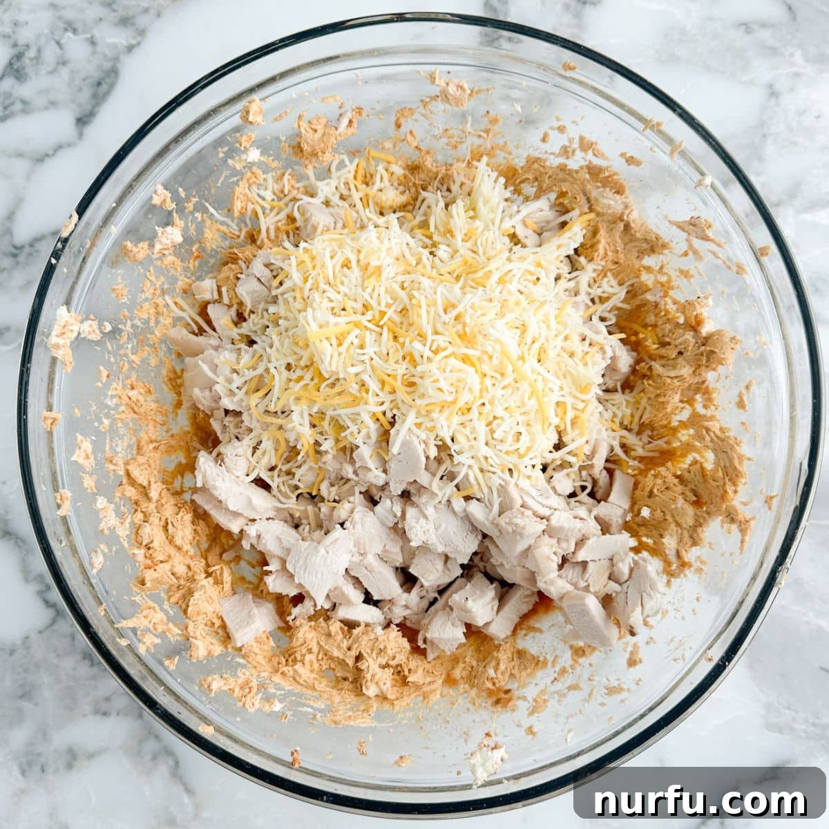 A large mixing bowl containing cream cheese, cooked shredded chicken, and shredded cheese, combined to create the flavorful filling for the bell peppers.