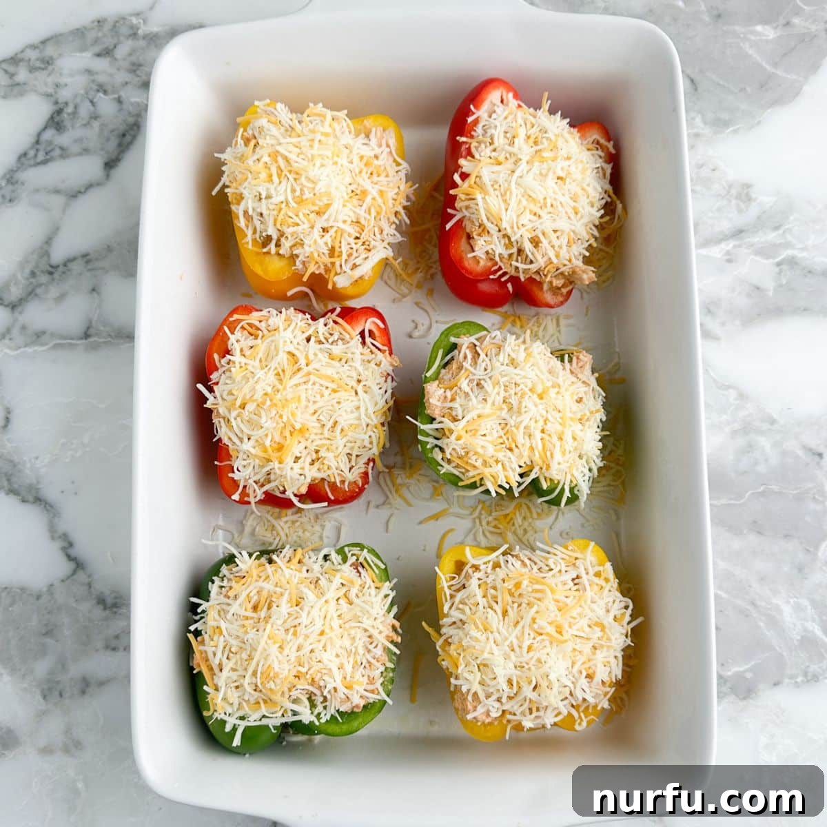 A casserole dish filled with chicken and cheese stuffed bell peppers, ready for baking, topped with an extra layer of shredded cheese.