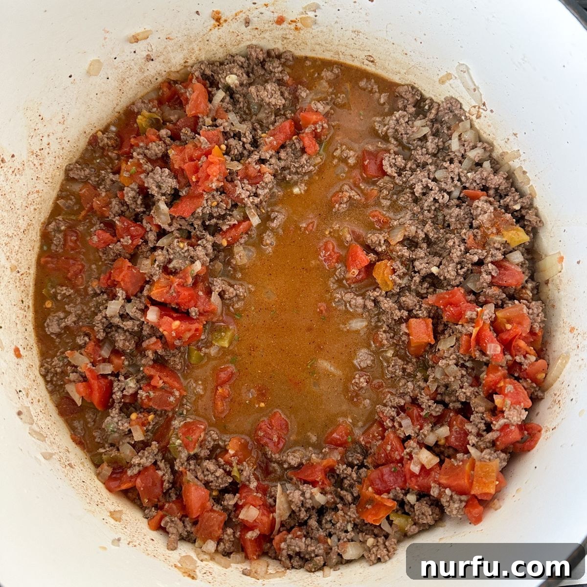 Southwestern Fiesta Soup 5 A pot on the stove with browned ground beef, onions, and garlic, now mixed with beef broth and diced tomatoes, creating the soup's aromatic base.
