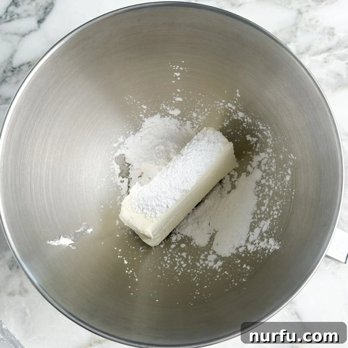 A mixing bowl holding a creamy blend of softened cream cheese, finely sifted powdered sugar, and a hint of vanilla, all whipped together to a smooth, inviting consistency.