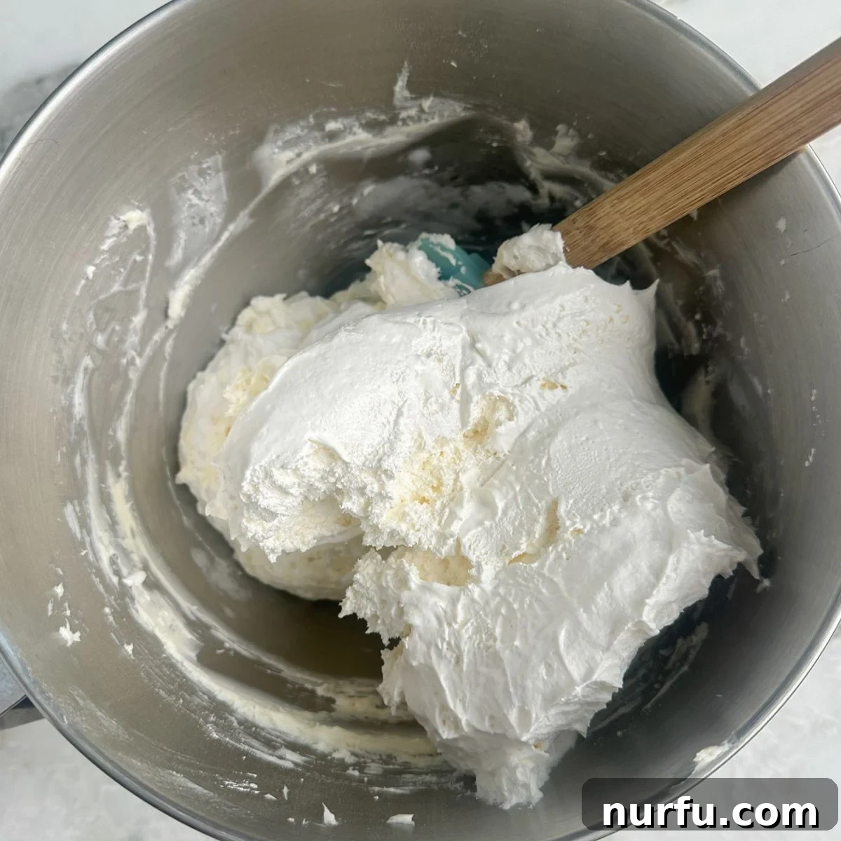 A partially mixed bowl showcasing the blending of Cool Whip and cream cheese, beginning to form a light and airy base for the easy pineapple dip.