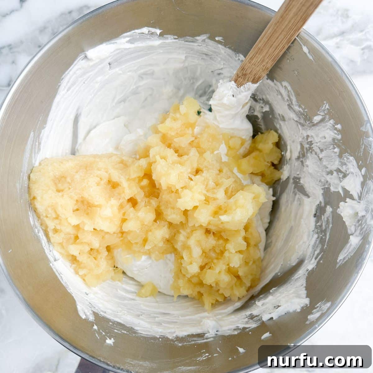 A bowl containing the rich, creamy base of the dip, with thoroughly drained crushed pineapple being delicately folded in, ensuring every spoonful will have a burst of tropical flavor.
