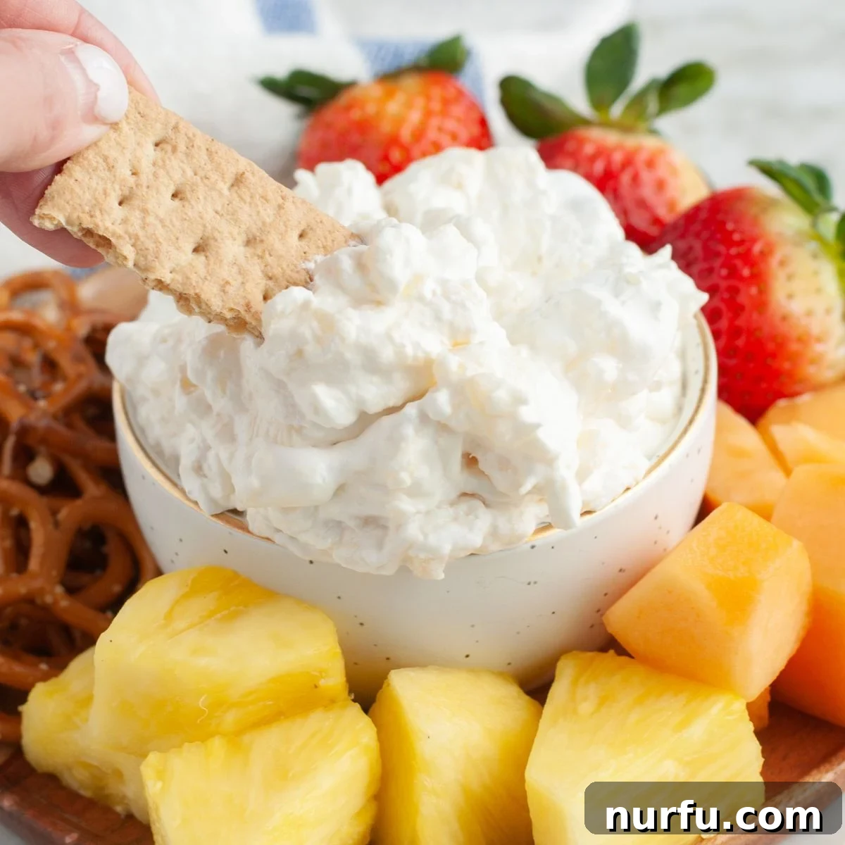 A beautifully presented bowl of creamy pineapple dip, served with a single crisp graham cracker dipped in, highlighting its smooth texture and inviting appeal.