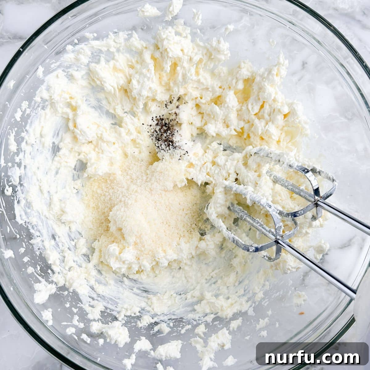 Irresistible Vidalia Onion Dip 4 A bowl of cream cheese and grated Parmesan cheese being mixed together with an electric hand mixer, creating a smooth, creamy base for the dip.
