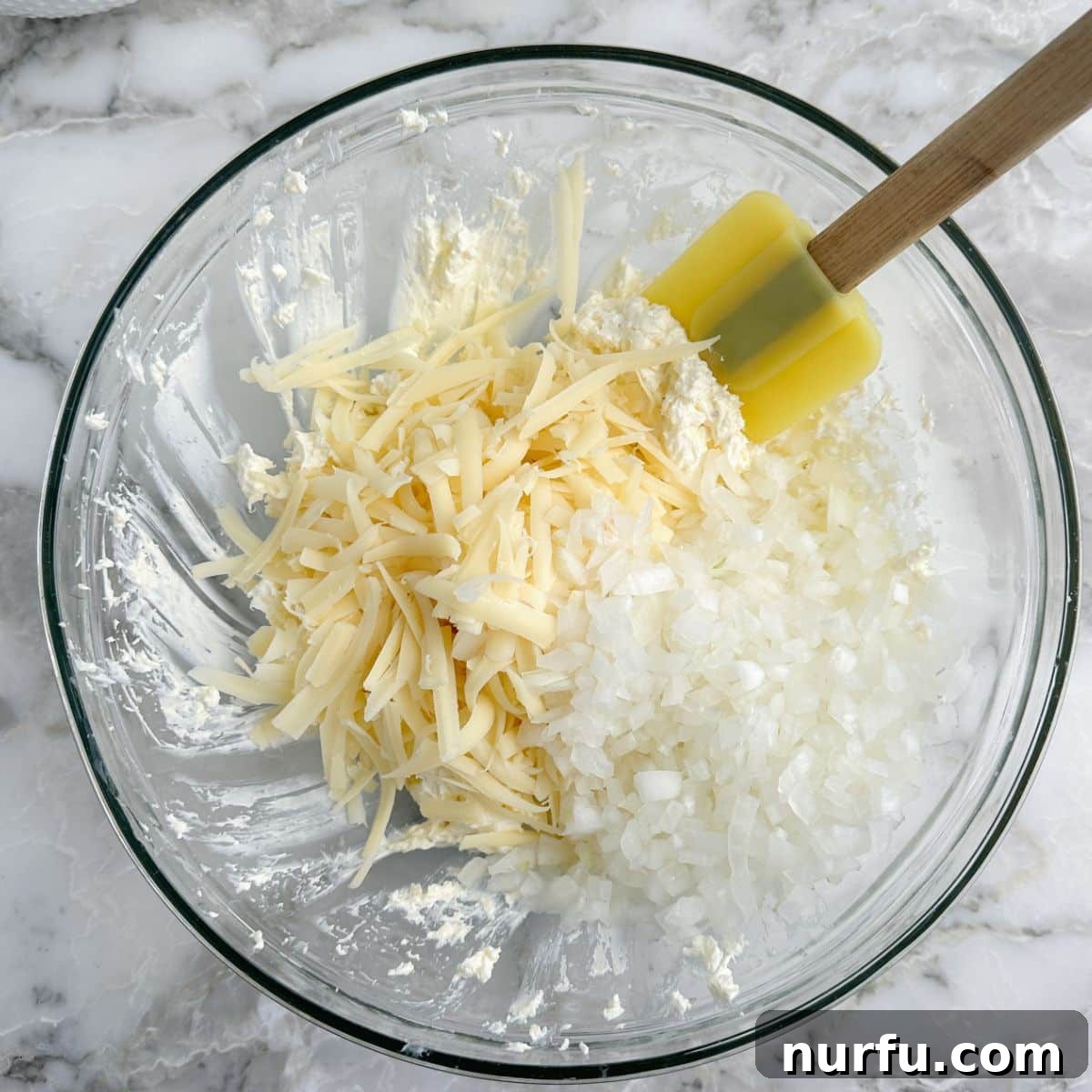 Irresistible Vidalia Onion Dip 5 A mixing bowl containing a creamy mixture of cream cheese and mayonnaise, with shredded Swiss cheese being added, illustrating a key step in preparing the onion dip.