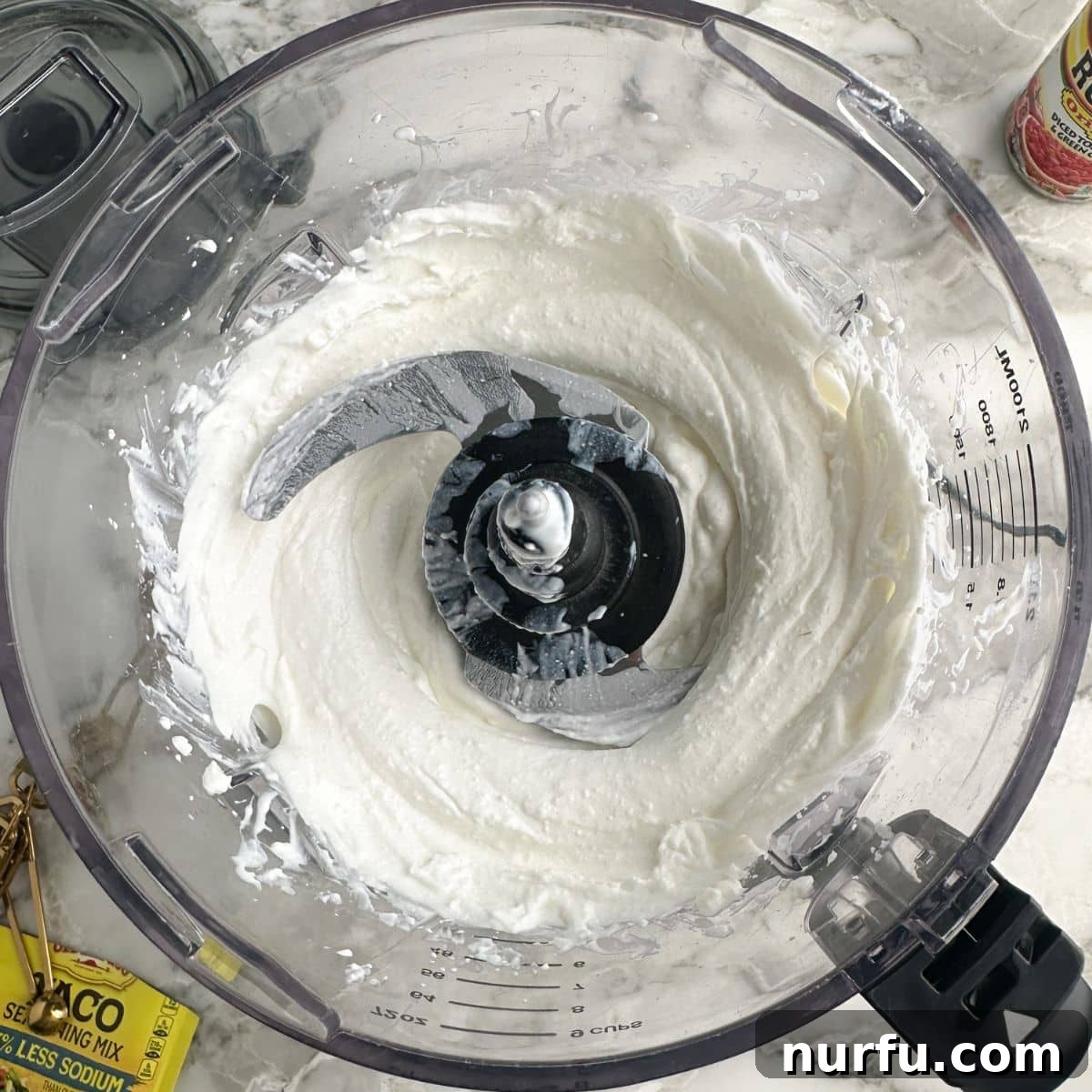 A close-up view inside a food processor bowl, showing cottage cheese that has been whipped to a perfectly smooth, creamy, and uniform consistency, ready for the next ingredients.