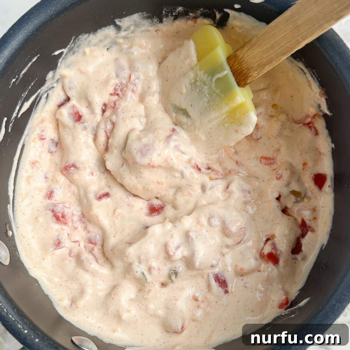 A freshly made bowl of cottage cheese queso, garnished with a sprinkle of fresh cilantro, with a spatula resting inside, inviting a taste. The dip looks rich and perfectly smooth.