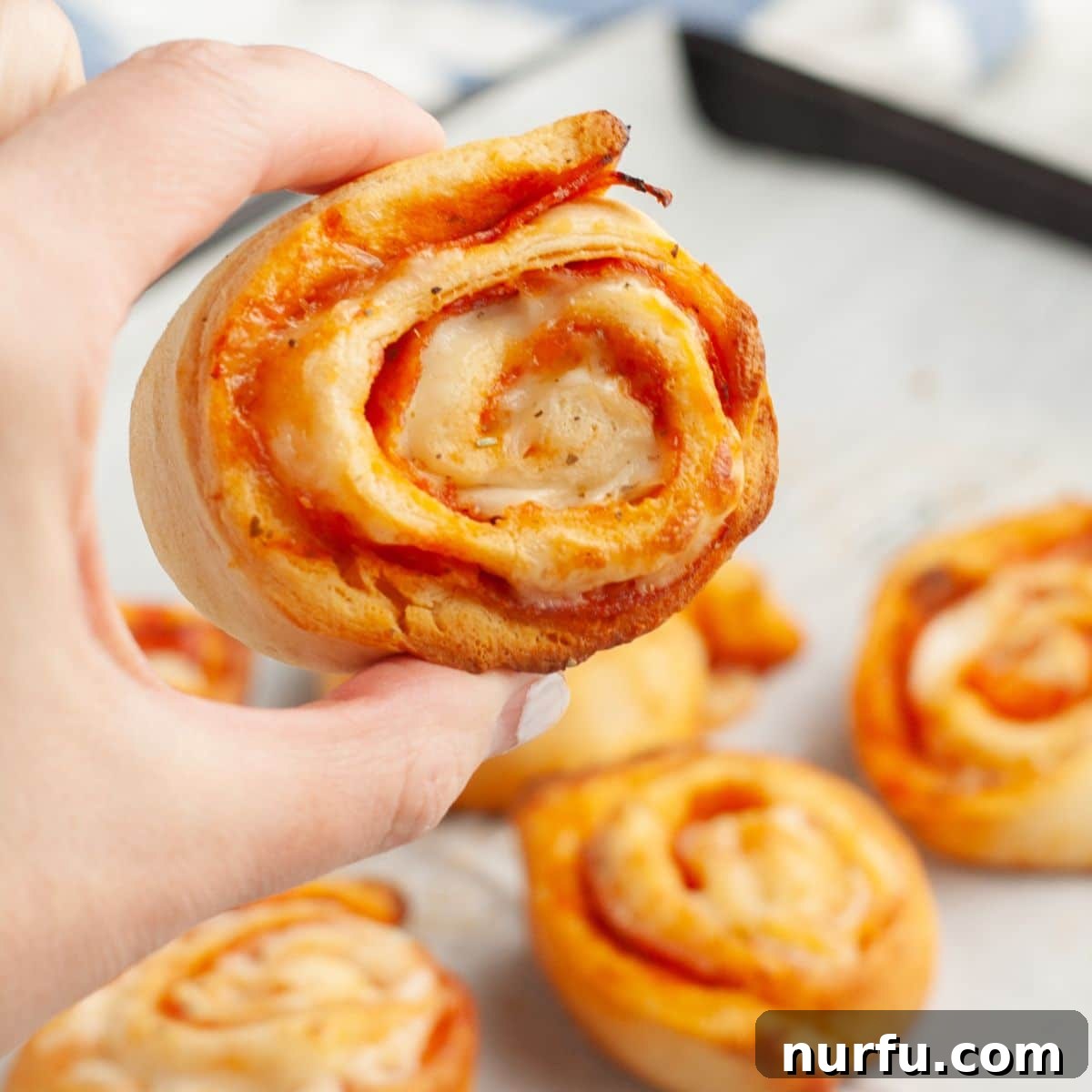 Pepperoni Pizza Swirls 11 A hand holds a perfectly baked pepperoni pinwheel, golden brown and cheesy, showcasing its inviting spiral layers.