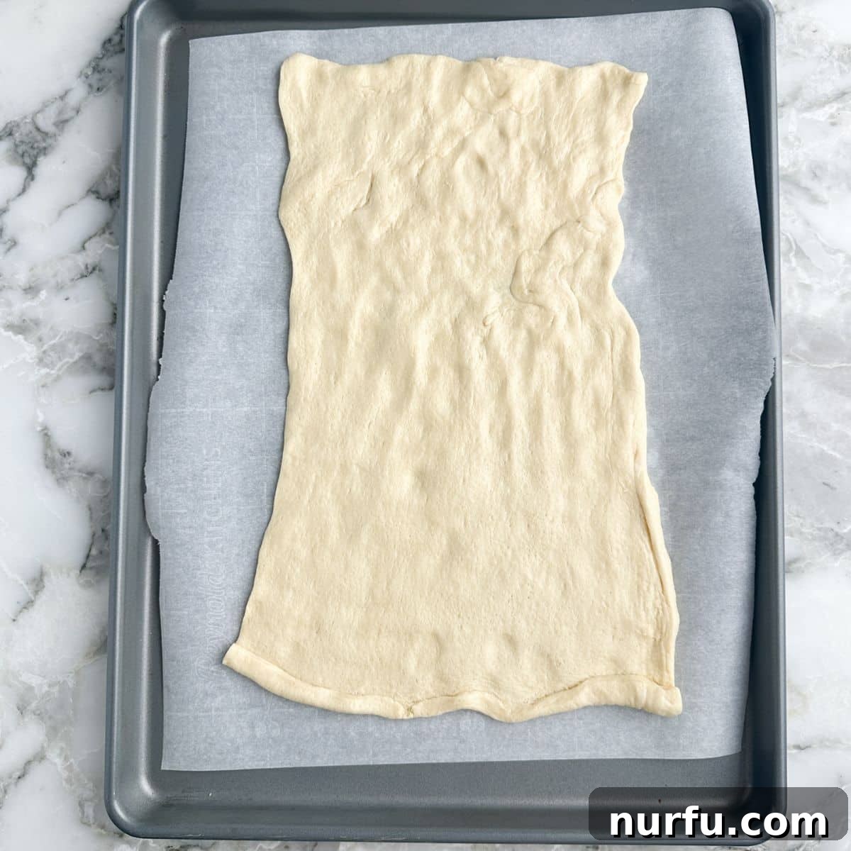 Pepperoni Pizza Swirls 4 Crescent dough unrolled and flattened on a parchment-lined baking sheet, ready for toppings.