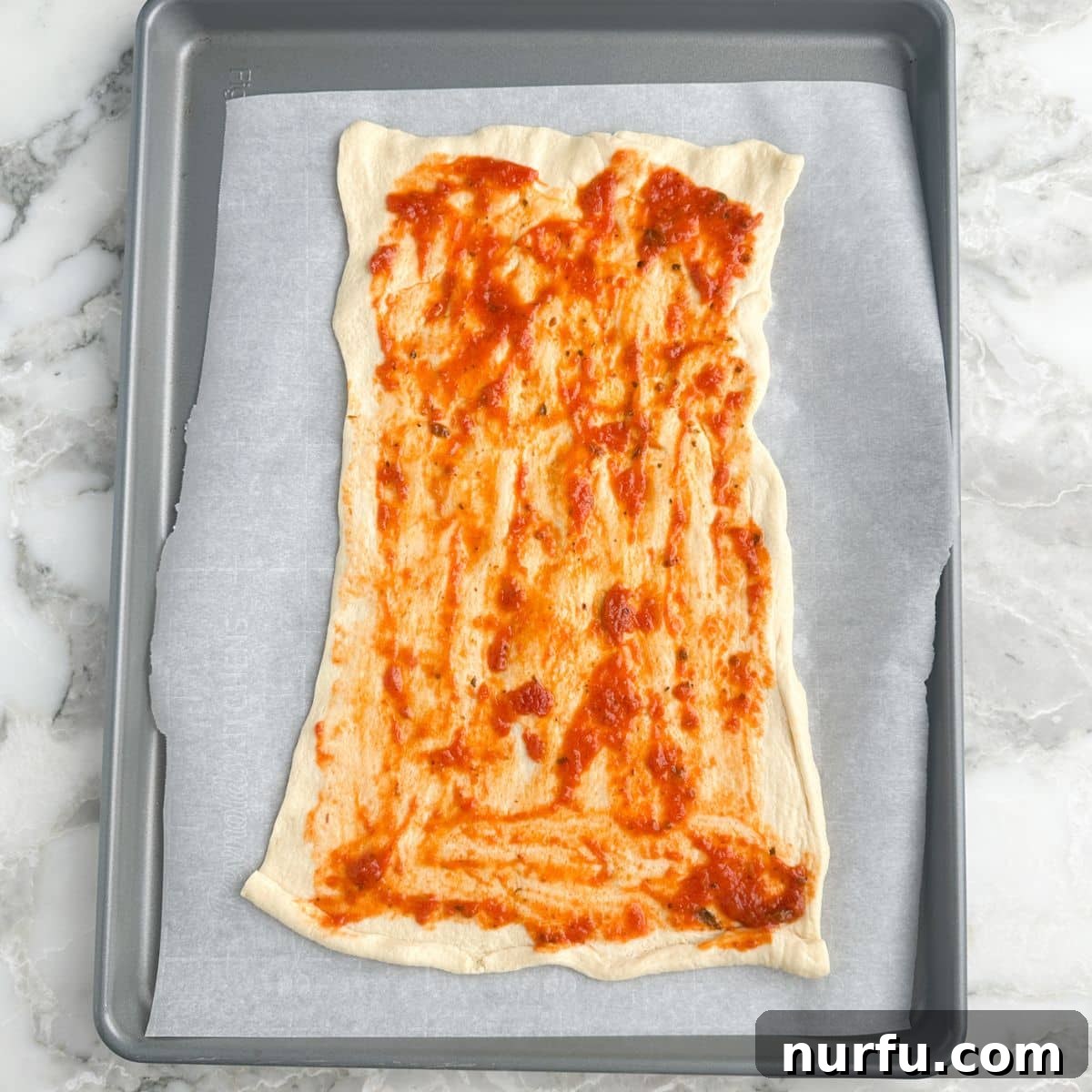 Pepperoni Pizza Swirls 5 Crescent roll dough topped with a thin layer of pizza sauce and Italian seasoning, prepared for the next layer of ingredients.