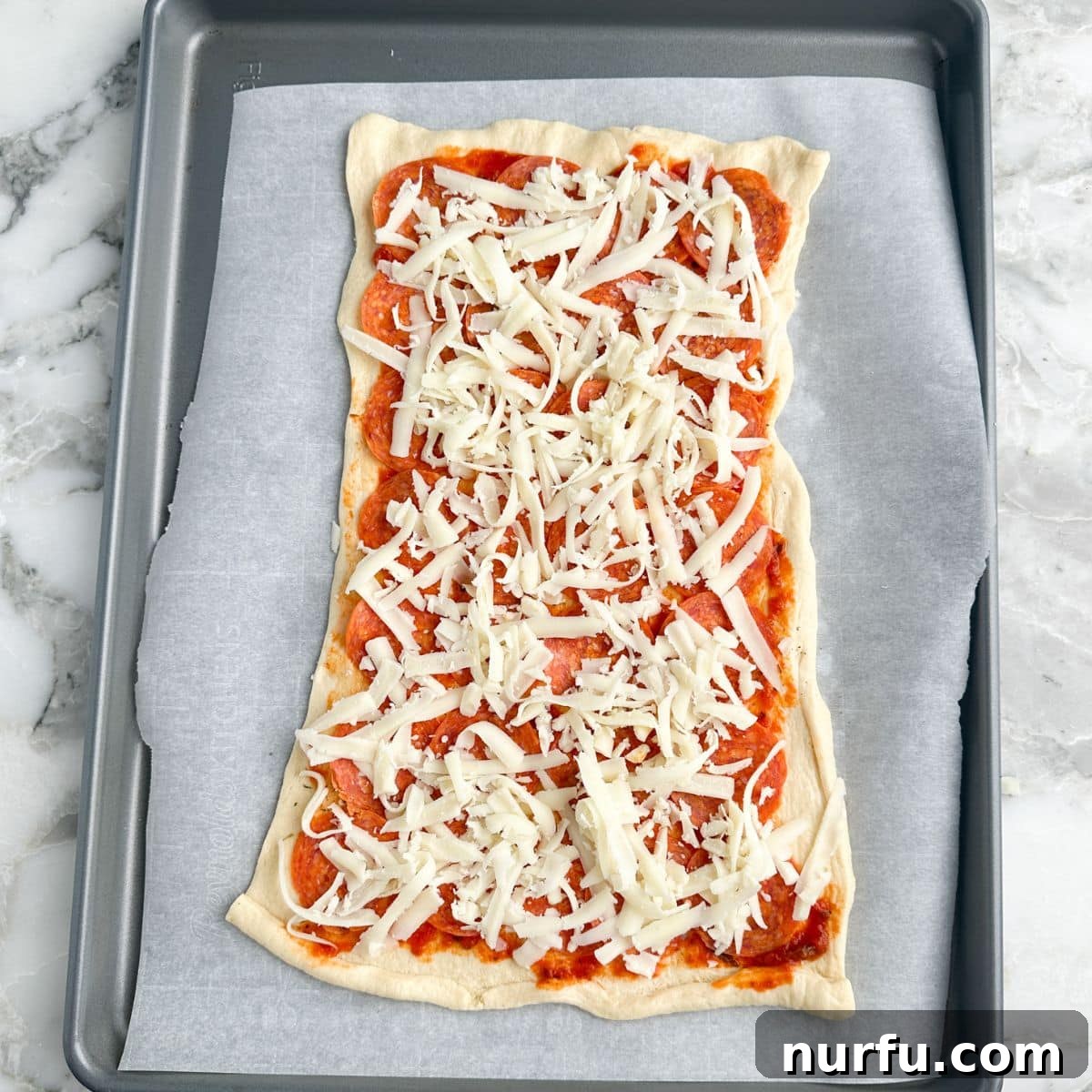 Pepperoni Pizza Swirls 7 Crescent roll dough topped with pizza sauce, pepperoni, and a generous layer of shredded mozzarella cheese, ready to be rolled.