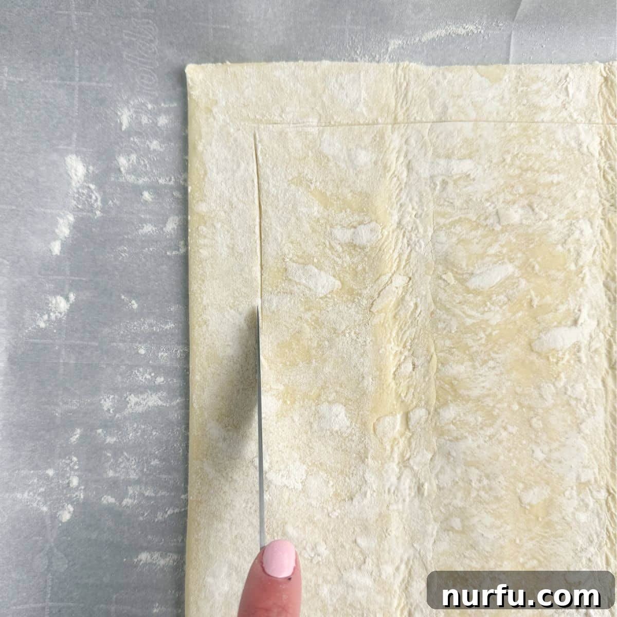 Quick Puff Pastry Pizza 4 A knife gently scoring the edges of thawed puff pastry dough on parchment paper, preparing it for the crust.