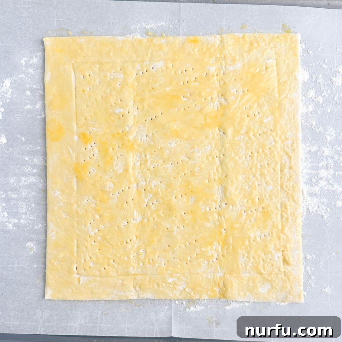 Quick Puff Pastry Pizza 6 Puff pastry dough on parchment paper, glistening with an even coat of egg wash before baking.