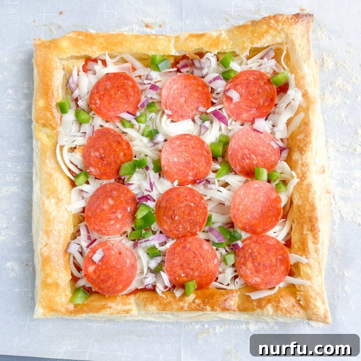 Quick Puff Pastry Pizza 8 A puff pastry pizza fully loaded with sauce, cheese, and various toppings, ready for its final bake.
