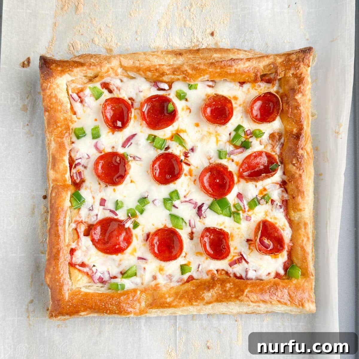 Quick Puff Pastry Pizza 9 A golden-brown puff pastry pizza, fresh out of the oven, with melted, bubbly cheese and vibrant toppings on a baking pan.