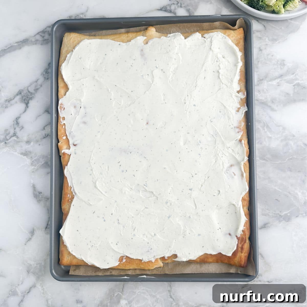 Flaky Garden Veggie Bake 7 The cooled crescent roll dough base with the creamy ranch spread evenly applied over its surface.