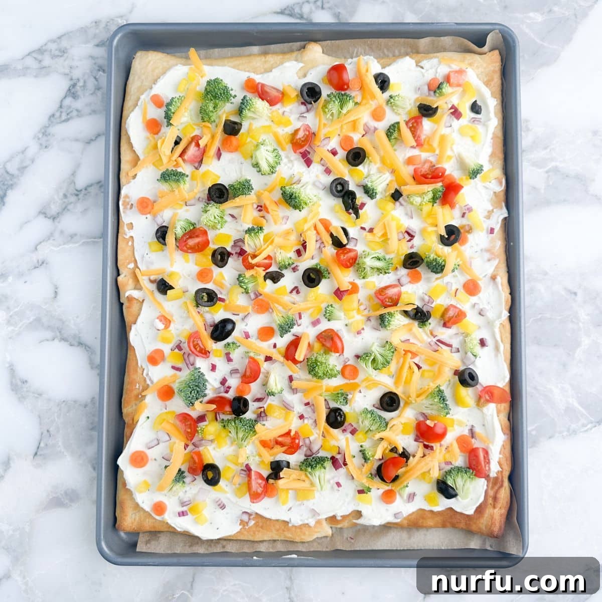 Flaky Garden Veggie Bake 8 A finished crescent roll vegetable pizza on a baking sheet, topped with colorful chopped vegetables and shredded cheese.