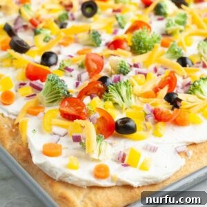 Crescent roll vegetable pizza in a pan, garnished with colorful vegetables.