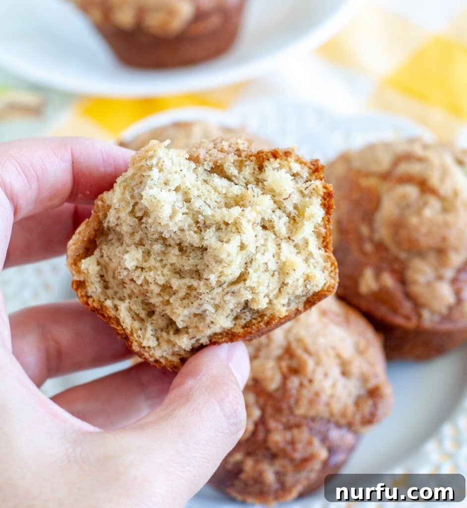 Bakery-Style Banana Bread Muffins 5 A hand holding a banana bread muffin, perfectly halved to show its moist interior.