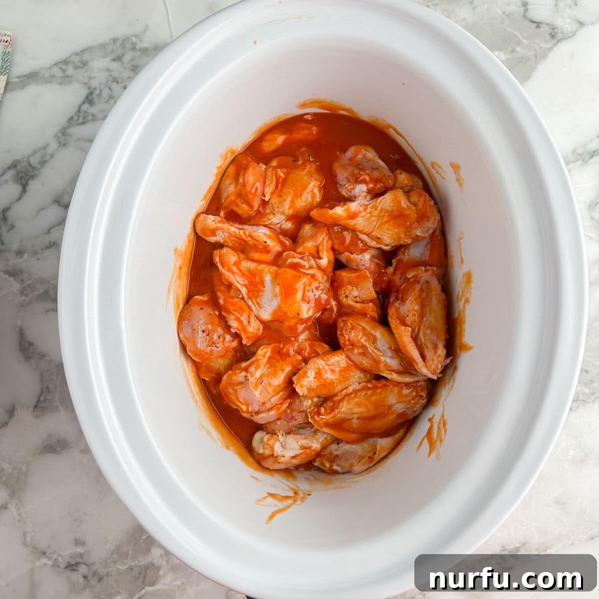 Effortless Slow Cooker Chicken Wings 7 Uncooked buffalo wings evenly coated in sauce and arranged inside a slow cooker, ready for cooking.