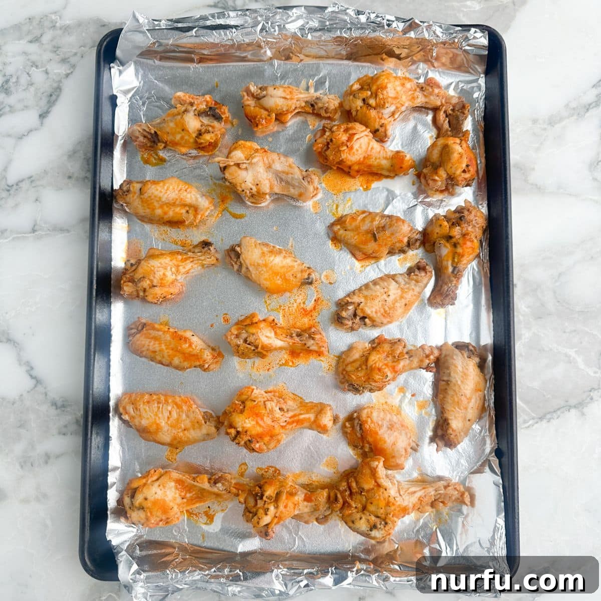 Effortless Slow Cooker Chicken Wings 8 Tender, cooked chicken wings neatly arranged in a single layer on a foil-lined baking dish, ready for broiling.