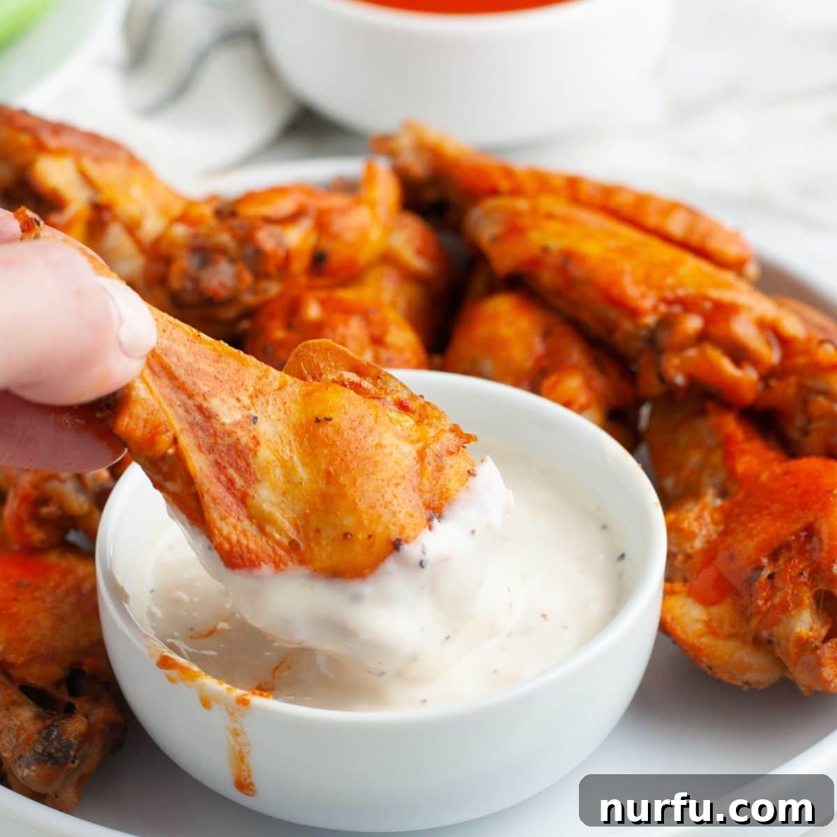 Effortless Slow Cooker Chicken Wings 10 A perfectly cooked chicken wing being dipped into a bowl of creamy ranch sauce, highlighting its tender texture.