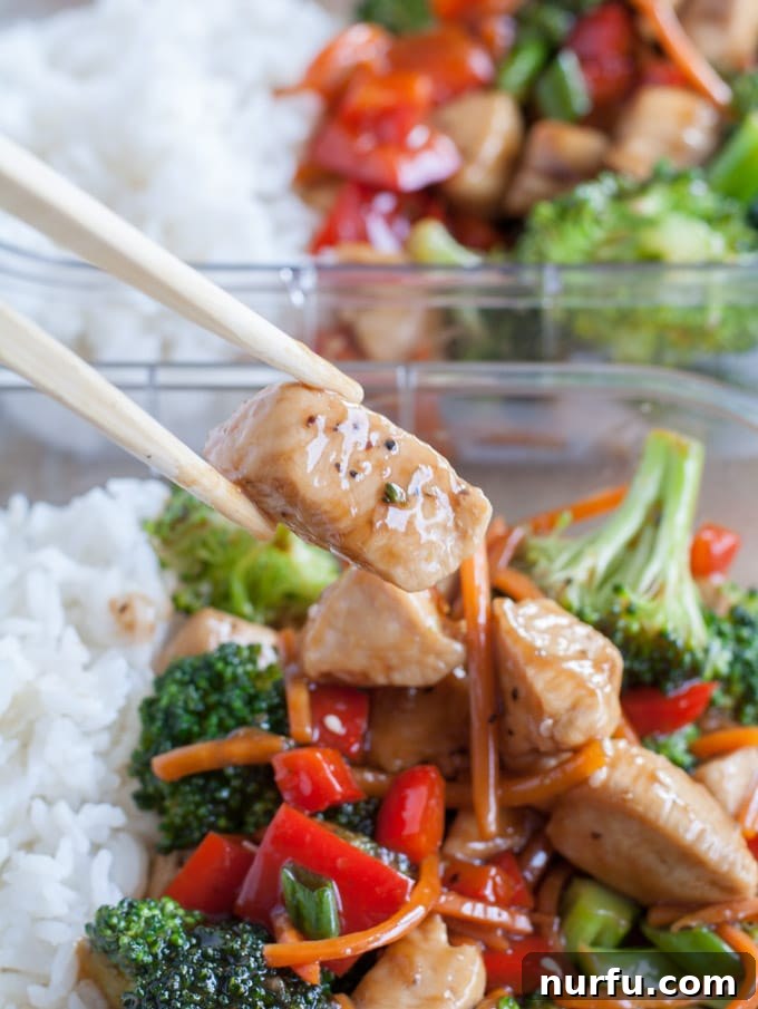 Chopsticks gently holding a piece of teriyaki chicken with bright green broccoli and red bell peppers, ready for a bite.