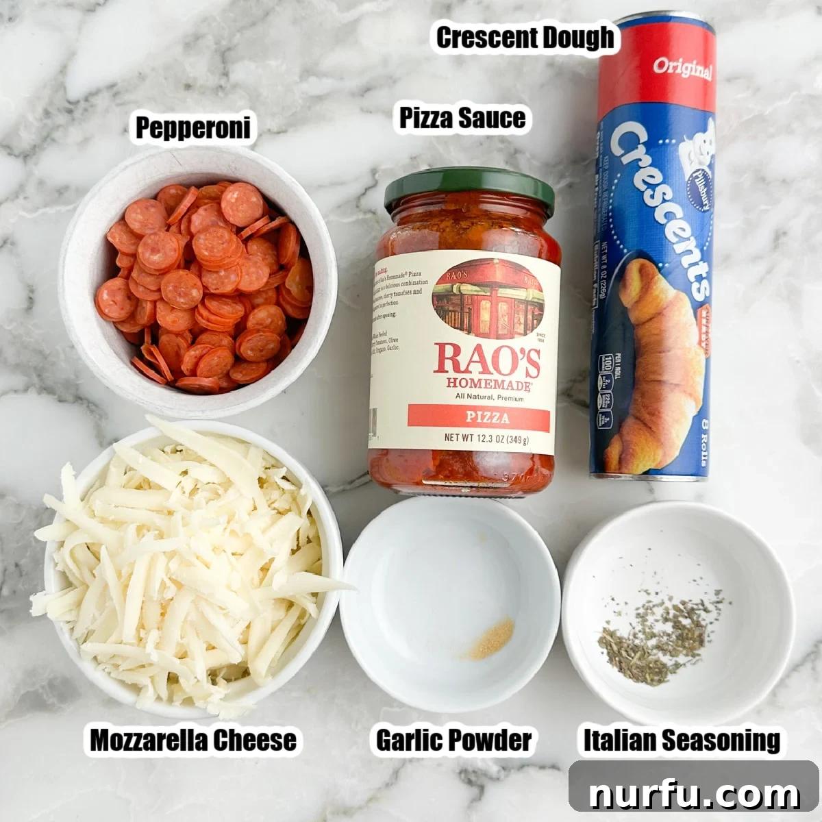 A vibrant flat lay showing key ingredients for pizza cupcakes: a bowl of shredded mozzarella, a pile of mini pepperonis, a jar of pizza sauce, unrolled crescent dough, and small dishes of garlic powder and Italian seasoning.