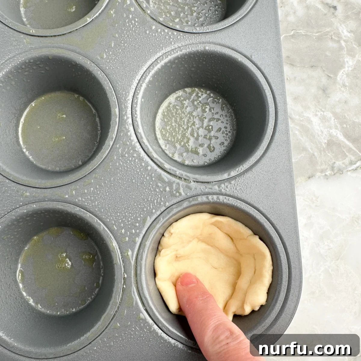 A non-stick muffin tin with crescent dough triangles pressed into each cup, forming the base of the pizza cupcakes.