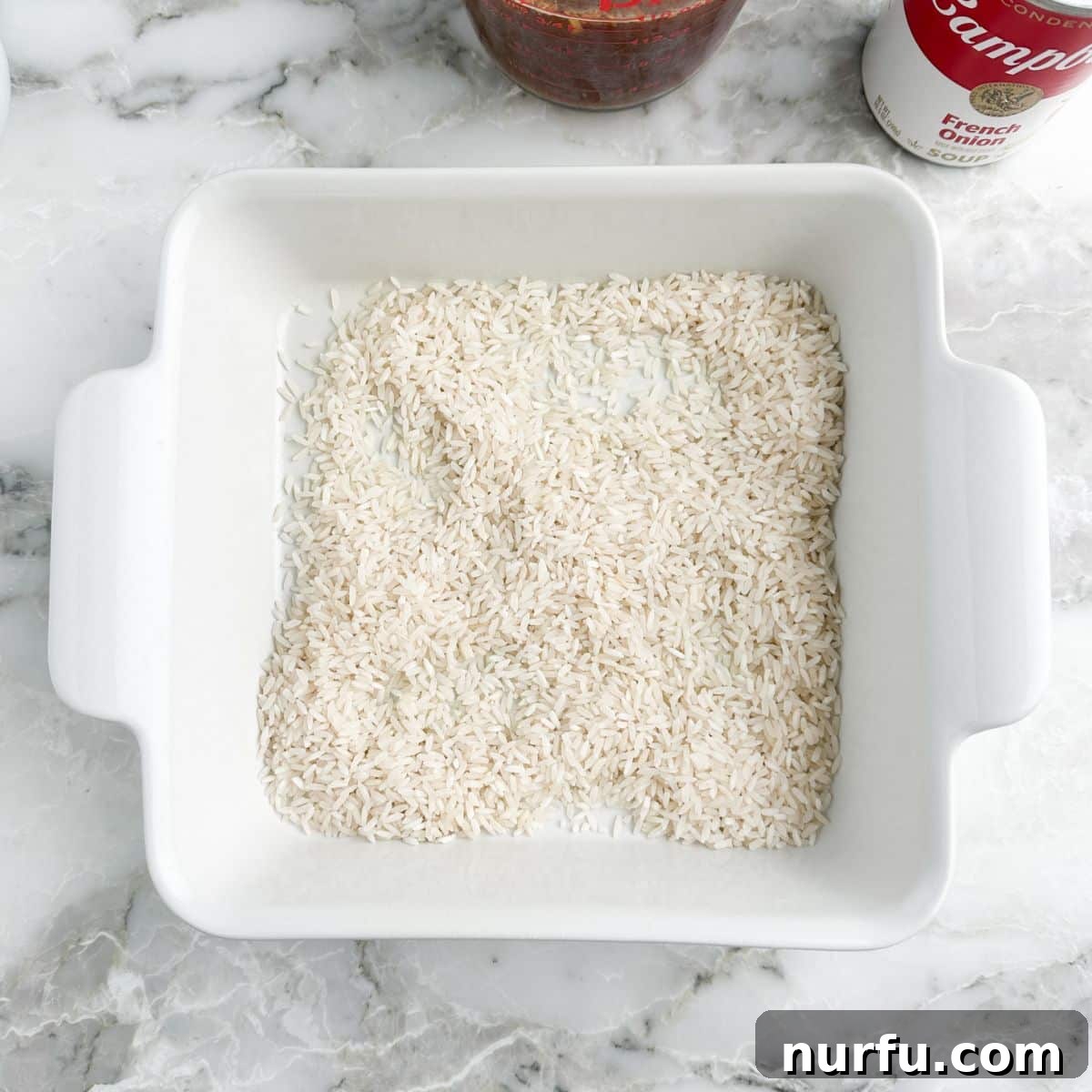 Caramelized Onion and Gruyere Rice 5 An 8x8 inch baking dish with an even layer of uncooked long-grain white rice spread across the bottom.