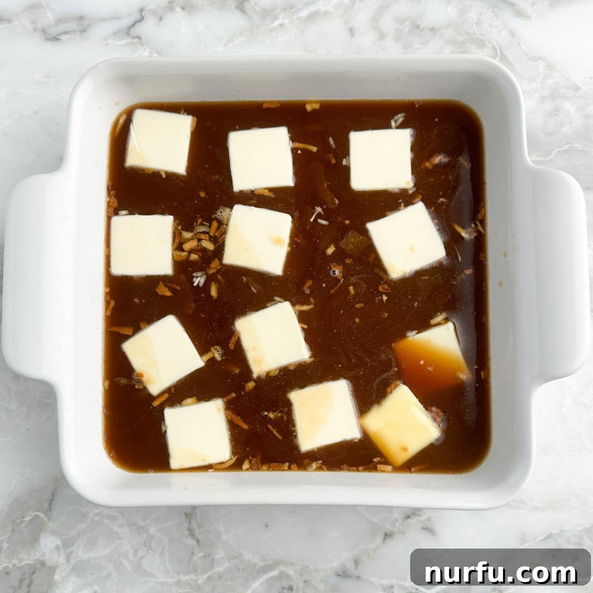 Caramelized Onion and Gruyere Rice 7 A baking dish with rice, French onion soup, and beef broth, topped with evenly spaced pats of butter, covered with foil for baking.